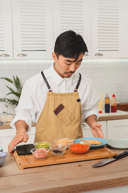 Japoński szef kuchni gotuje sushi w białej kuchni. Składniki sushi robią to samemu