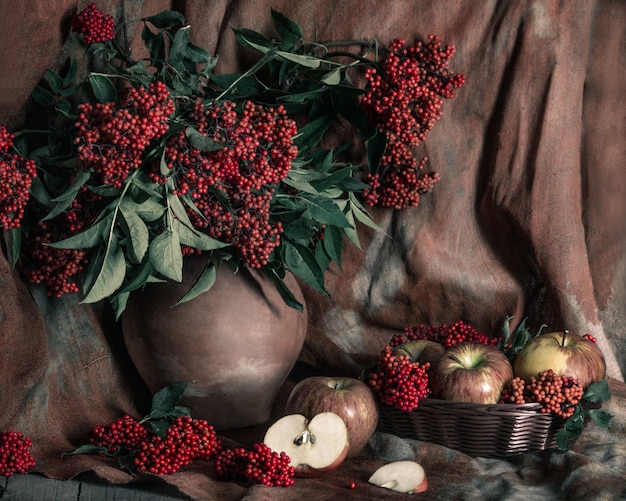 Zdjęcie jaskrawy czerwony elderberry w starym glinianym garnku i jabłkach na stole z starym tekstylnym tłem. martwa natura w stylu vintage