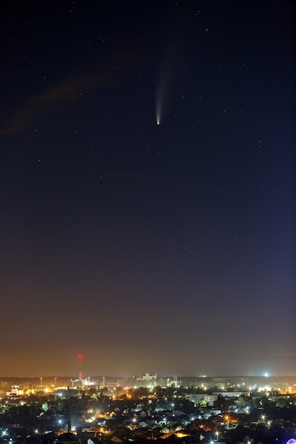 Jasna kometa NEOWISE na rozgwieżdżonym nocnym niebie Obiekt kosmiczny nad miastem z oświetleniem ulicznym