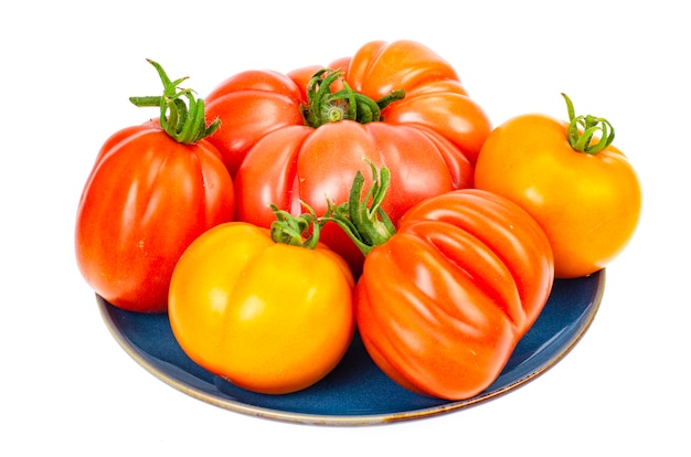 Jasne kolorowe pomidory na talerzu na białym tle.