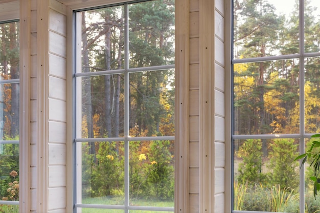 Jasne wnętrze pokoju w drewnianym domu z dużym oknem wychodzącym na jesienny dziedziniec. Złoty jesienny krajobraz w białym oknie.