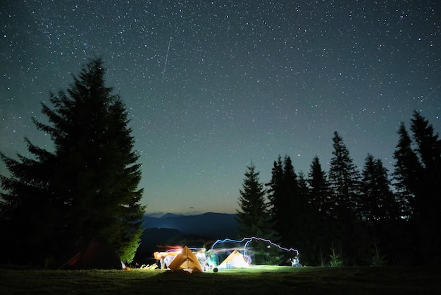 Jasno oświetlone namioty kempingowe świecące na kempingu w ciemnych górach pod nocnym niebem pokrytym gwiazdami. Koncepcja aktywnego stylu życia i podróży.