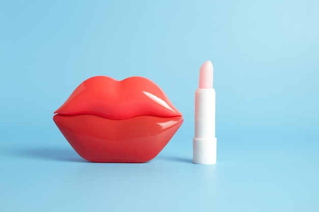 Jasnoczerwone plastikowe kobiece usta i higieniczna szminka na jasnoniebieskim tle Pielęgnacja skóry warg Koncepcja kosmetyków kosmetycznych