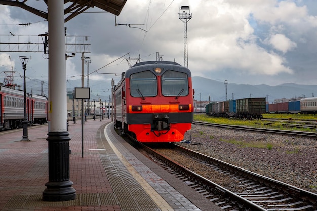Jasnoczerwony pociąg podjeżdża pod peron dworca kolejowego w mieście Transport pasażerski