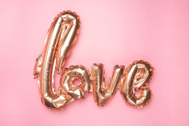 Jasnoróżowe balony foliowe w kształcie słowa miłość z sercami na różowym tle