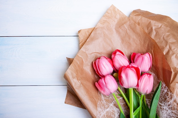 Zdjęcie jasnoróżowe tulipany leżą na papierze pakowym na jasnoniebieskim drewnianym tle. widok płaski, widok z góry