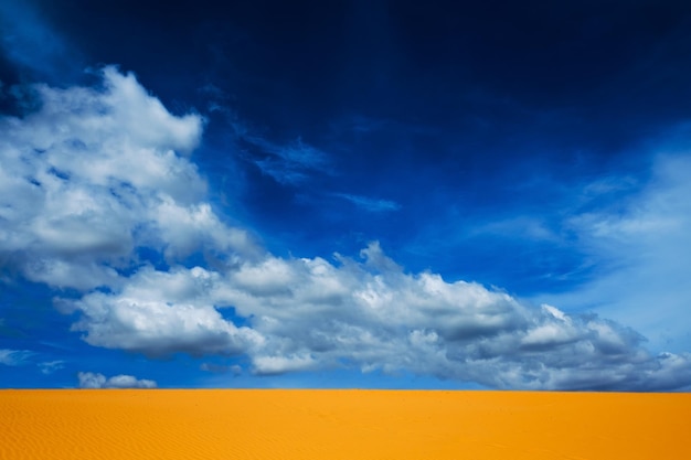 Jasnożółty piasek opróżnia się na tle błękitnego nieba z chmurami