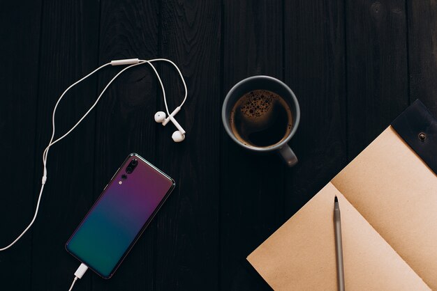 Jasny kolorowy smartfon na czarnym drewnianym stole. Poranna kawa.