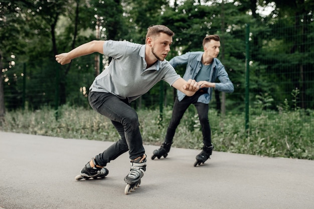 Jazda na rolkach, dwóch łyżwiarzy płci męskiej rozpoczyna wyścig prędkości w letnim parku. Miejska jazda na rolkach, aktywny sport ekstremalny na świeżym powietrzu, jazda na rolkach