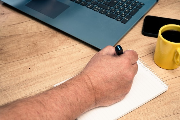 Jeden człowiek robi notatki w notatniku obok swojego laptopa podczas pracy w domu lub biurze. Koncepcja technologii, biuro domowe
