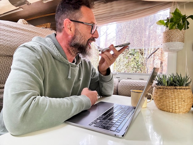 Jeden podróżny mężczyzna używający laptopa w przyczepie kempingowej w połączeniu telefonicznym w roamingu Podróżny i mały biznes zarobki z mediów społecznościowych Ludzie i technologia Podróż Nomadyczny styl życia dorosły mężczyzna