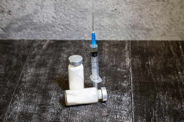 Jedna medyczna ampułka ze szklaną butelką i medyczna jednorazowa strzykawka z igłą. Koncepcja medyczna przedstawia medyczną probówkę i szczepionki przeciwko wirusowi. ciemny drewniany stół