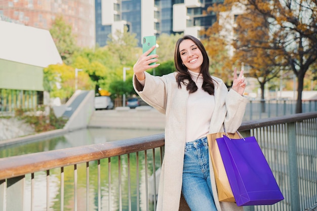 Jedna młoda, piękna, szczęśliwa kobieta uśmiecha się, robiąc portret selfie po zakupach i udostępnianiu