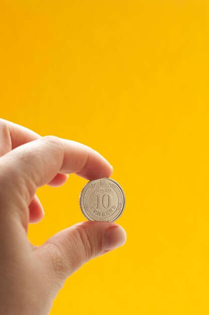 jedna moneta na żółtym tle w ręku pieniądze waluta metaliczny hrywna finanse skrytka inwestycje