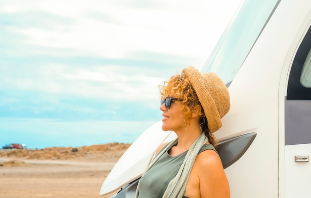 Jedna podróżująca samotnie kobieta cieszy się miejscem docelowym, stojąc przed nowoczesnym, dużym pojazdem kempingowym, kamperem, podziwiając krajobraz pustynnej przyrody wokół Błękitne niebo w tle Styl życia kobiety