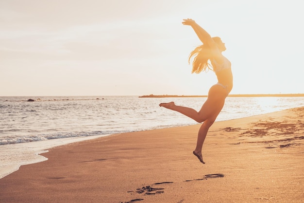 Jedna szczęśliwa i zdrowa młoda kobieta skacząca po piasku na plaży bawiąca się i ciesząca się latem na świeżym powietrzu Piękna atrakcyjna dziewczyna gra