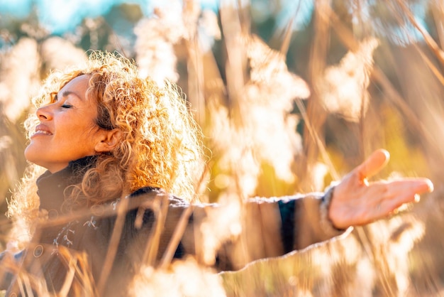 Zdjęcie jedna szczęśliwa kobieta rozciągająca ramiona na wysokim żółtym trawiastym polu w złotym świetle słońca uśmiechając się i oddychając, ciesząc się naturą i kochając środowisko i zrównoważony rozwój ludzie kobiecy styl życia sukces