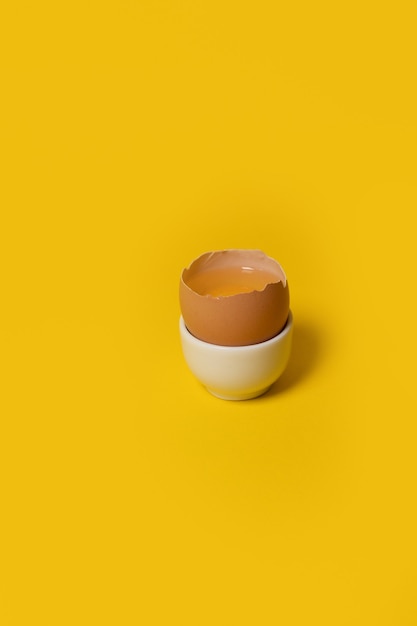 Jedno brązowe jajko kurze w kubku jajka na żółtym tle minimalna koncepcja wielkanocna