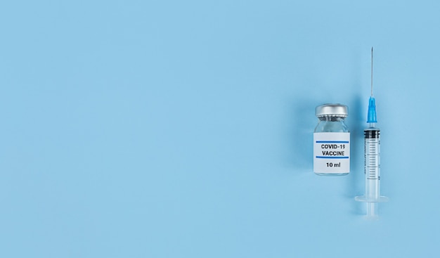 Jednorazowa strzykawka i butelka medyczna ze szczepionką przeciwko koronawirusowi na niebieskim tle z miejscem na kopię.