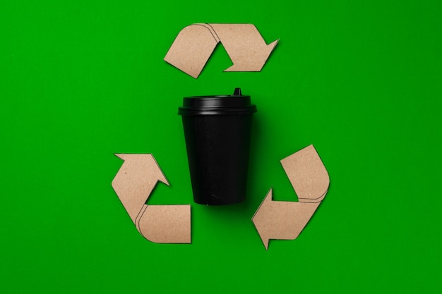 Zdjęcie jednorazowe filiżanki kawy i znak recyklingu na zielonym tle