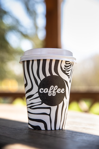 Zdjęcie jednorazowy kubek na wynos z kawą na drewnianej ławce w porannym ogrodzie