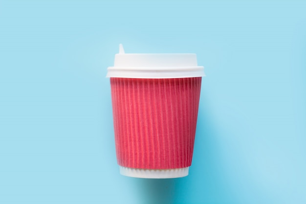 Jednorazowy papierowy czerwony kubek z białą plastikową pokrywką na gorącą kawę lub herbatę na niebiesko.
