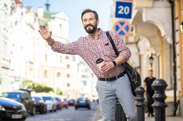 Jedź. Przyjemny przystojny mężczyzna stojący na ulicy podczas zatrzymywania samochodu