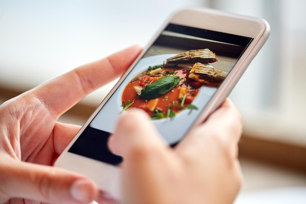 Zdjęcie jedzenie, jedzenie, technologia, koncepcja kulinarna i ludzie - ręce kobiety ze zdjęciem zupy gazpacho na ekranie smartfona w restauracji