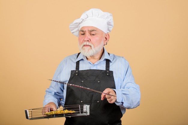 Jedzenie na grillu Koncepcja pikniku i grilla Koncepcja grilla Dojrzały brodaty szef kuchni trzyma kratkę do grillowania Smaczne i pyszne naczynia do grillowania Zdrowy sposób odżywiania Grill i wędzone danie