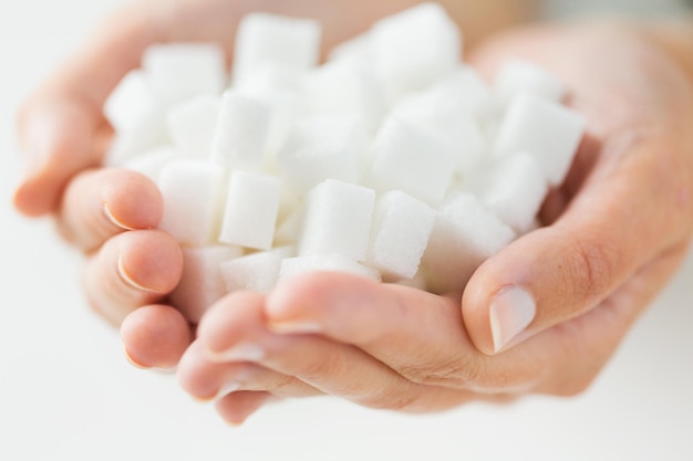 jedzenie, niezdrowe jedzenie, cukrzyca i niezdrowe jedzenie koncepcja - zbliżenie białego cukru w kostkach w rękach kobiety