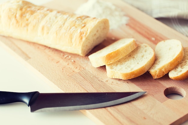 jedzenie, niezdrowe jedzenie, dieta i niezdrowe jedzenie koncepcja - zbliżenie białego chleba lub bagietki i nóż kuchenny na drewnianej desce do krojenia