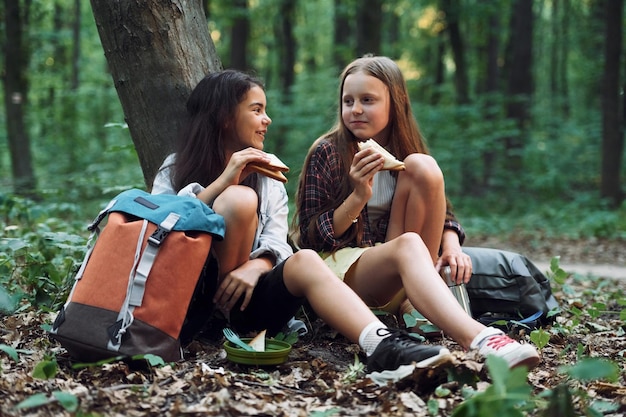 Jedzenie za pomocą plastikowych widelców i talerzy Dwie dziewczyny spędzają wolny czas w lesie, odkrywając nowe miejsca