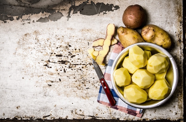 Zdjęcie jedzenie ziemniaczane. obrane ziemniaki w metalowej misce na rustykalnym stole. wolne miejsce na tekst. widok z góry