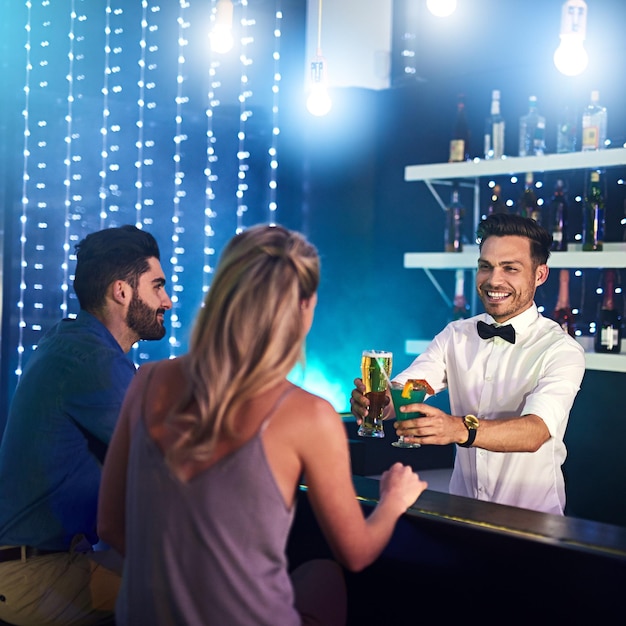 Jego umiejętności i osobowość sprawiają, że klienci są zadowoleni Ujęcie szczęśliwego barmana serwującego drinki parze w nocnym klubie