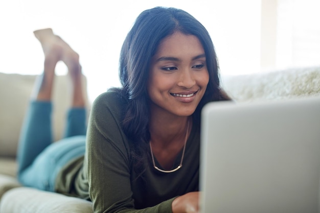 Jej kanały w mediach społecznościowych brzęczą Ujęcie atrakcyjnej młodej kobiety korzystającej z laptopa leżącej na sofie w domu