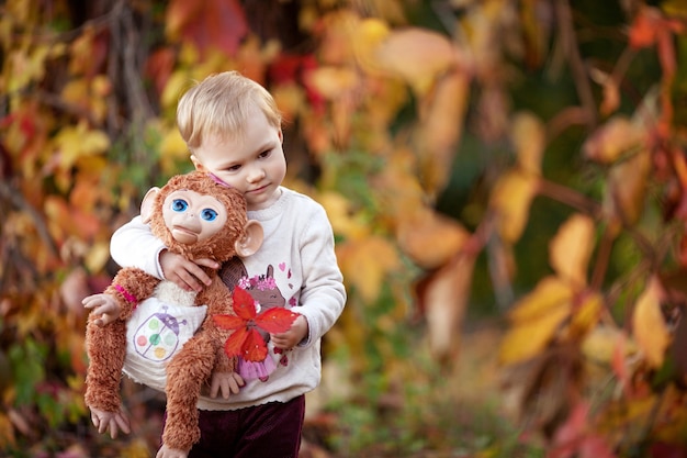 Jesień Emocjonalny Portret Dziewczynki. Całkiem Mała Dziewczynka Z Małpą Zabawką W Jesiennym Parku. Jesienne Zajęcia Dla Dzieci. Halloween I święto Dziękczynienia Zabawa Dla Rodziny.