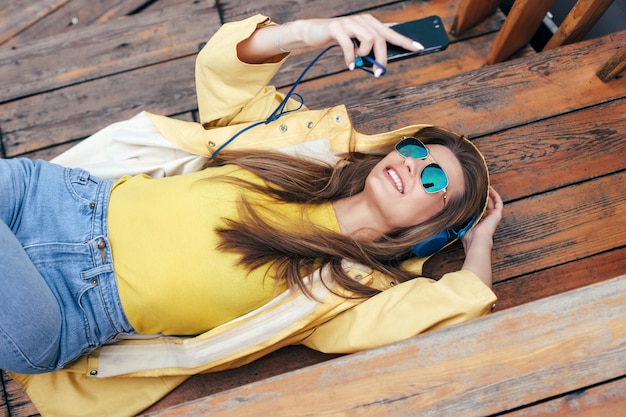 Zdjęcie jesień miasto styl szczęśliwa kobieta zabawy na ulicy słuchania muzyki z słuchawki i jej smartphone