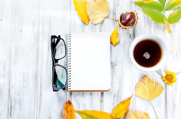 Jesień życia z filiżanką herbaty z ciasteczkami, pustym notatnikiem, okularami i liśćmi na białym tle drewnianych