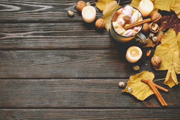 Zdjęcie jesieni tło robić wysuszeni spadków liście, kubek kakao z marshmallows, dokrętkami, cynamonem, szkocką kratą, jabłkami. widok z góry na brązowe drewno