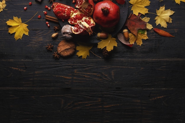 Jesienna kompozycja. Granat z orzechami, przyprawami i suchymi liśćmi na ciemnym drewnianym stole. Widok z góry.