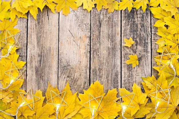 Zdjęcie jesienne tło z żółtymi liśćmi na drewnianym tle z girlandą w kształcie gwiazd