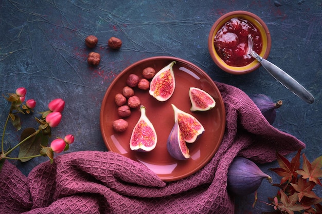 Jesienne tło ze świeżymi przekrojonymi na pół owocami figi na ceramicznym talerzu z terakoty Magenta ręcznik i czerwony klon Jesienne liście na ciemnofioletowej desce Dżem figowy w ceramicznej misce