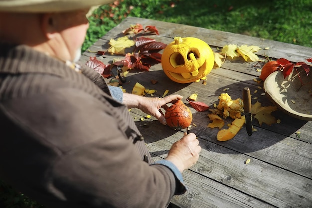 Jesienne tradycje i przygotowania do święta Halloween. Dom w naturze, przy stole wycina się lampa z dyni.