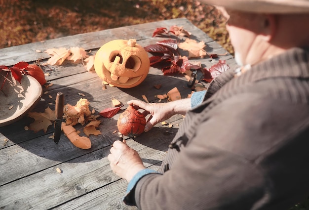 Jesienne tradycje i przygotowania do święta Halloween. Dom w naturze, przy stole wycina się lampa z dyni.