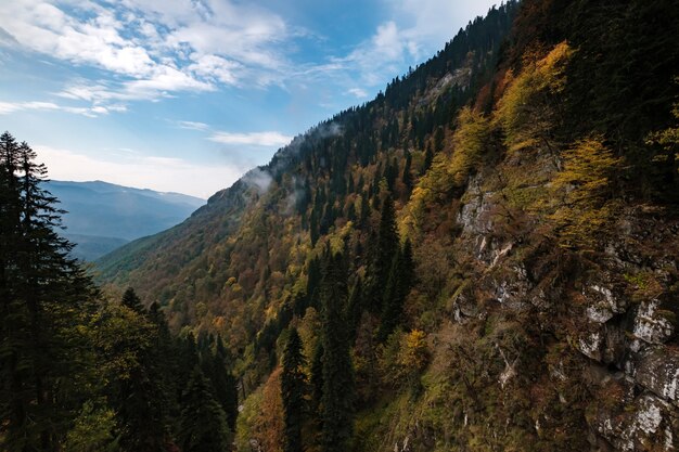 Jesienny krajobraz górski z kolorowym lasem i wysokimi szczytami Kaukazu. Ośrodek narciarski Rosa Khutor poza sezonem, Rosja, Soczi. Taniec chmur w górach