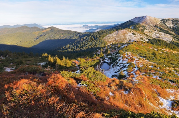 Jesienny krajobraz w górach. Pierwszy śnieg na stoku. Małe jezioro pokryte jest lodem. Karpaty, Ukraina, Europa