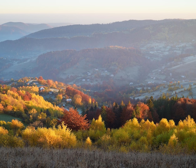 Jesieński krajobraz z lasem liściastym i widokiem na górską wioskę