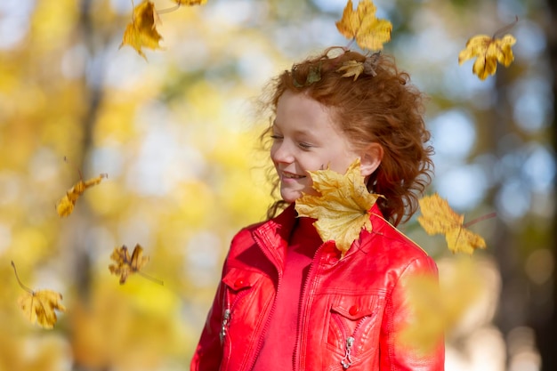 Jesieński portret uroczej uśmiechniętej dziewczynki z czerwonymi włosami z liśćmi klonu na świeżym powietrzu