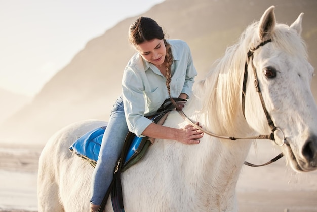 Jeździec na plaży i kobieta jadąca na koniu na świeżym powietrzu w letni poranek na trening lub trening Zachód słońca w naturze i młody jeździec na koniu ze swoim zwierzątkiem nad oceanem lub morzem, aby się zrelaksować