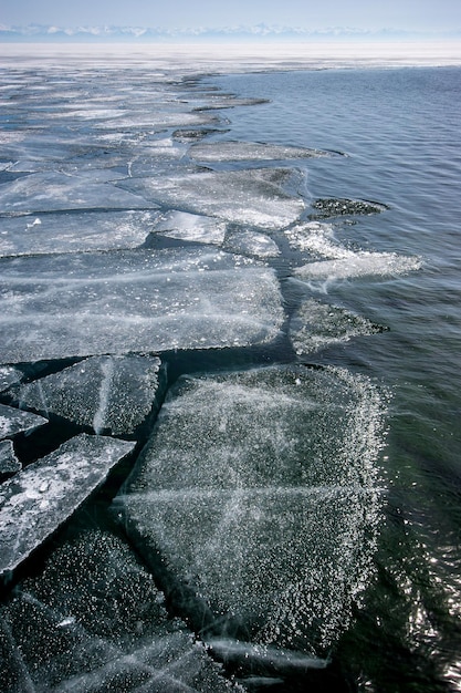 Jezioro Bajkał zimą z otwartą wodą i krawędzią pękniętego lodu Na horyzoncie widać pasmo górskie Orientacja pionowa